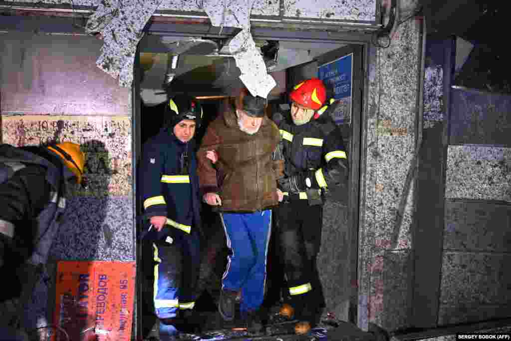 Рятувальники допомагають чоловікові покинути пошкоджений житловий будинок. Тисячі жителів залишилися без світла після того, як попередній російський удар пошкодив електричну інфраструктуру Харкова