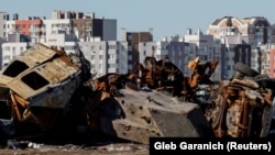 Цивільні автомобілі й військова техніка, знищені під час нападу Росії на Україну, перед житловими будинками в місті Буча, 30 березня 2023 року