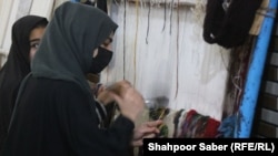 دو تن از دختران دانش آموز در هرات که در کارگاه قالین بافی کار می کنند
