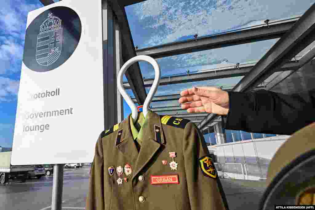 Wengriýanyň &quot;Ujratervezes&quot; (&ldquo;Gaýtadan işleniş&rdquo;) guramasynyň aktiwisti Budapeşt aeroportynda, Wengriýanyň hökümetiniň garaşylýan resmi otagyna girelgesiniň öňünde, &quot;Orbán&quot; diýen ýazgyly rus harby eşigini saklap dur.