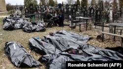 Поліцейські поруч із тілами загиблих під час російської окупації Бучі на місцевому кладовищі, квітень 2022 року