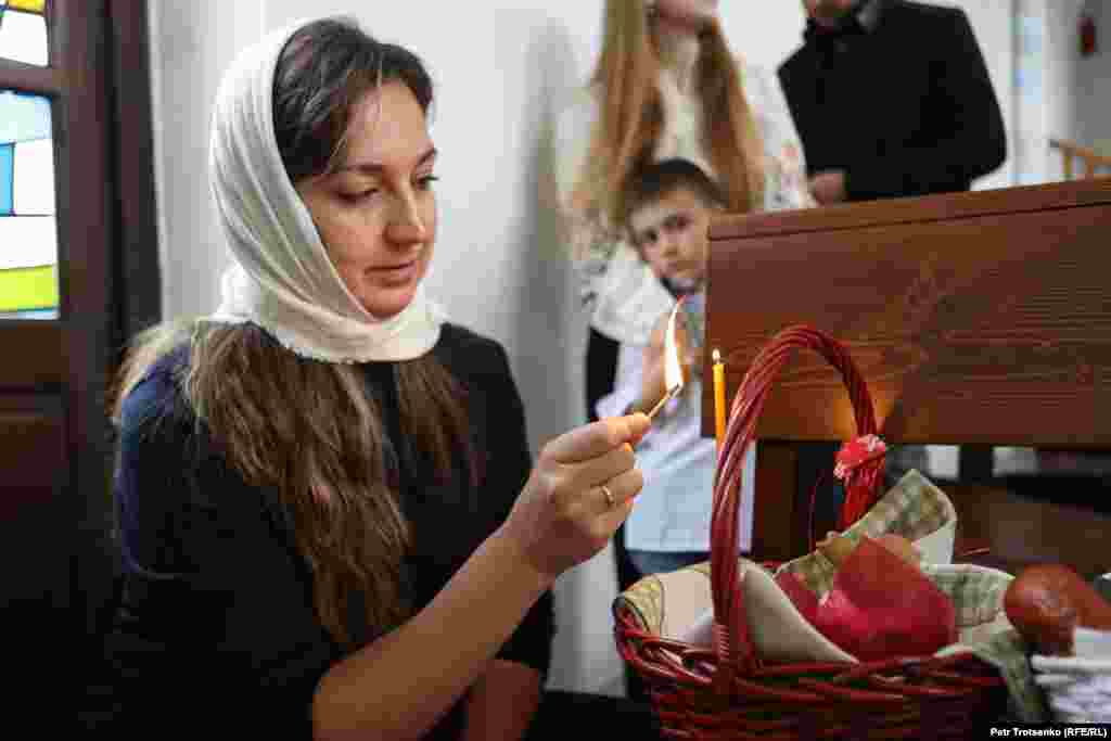 Женщина зажигает церковную свечу на куличе перед обрядом освящения