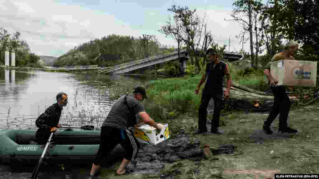 Безробітний Микола (другий праворуч) тепер перевозить ящики з їжею, яку привозять волонтери. Міст через річку Сіверський Донець, через який колись жителі села ходили на роботу, &ndash; тепер під водою