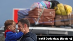 ARMENIA -- A refugee from Nagorno-Karabakh holds a child while standing next to a car upon their arrival in the border village of Kornidzor,, September 26, 2023.