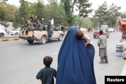 Ооганстандык аял балдарын көтөрүп баратат. Сүрөт иллюстрация үчүн колдонулду.