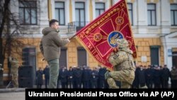 A Ukrainian Army officer kisses the flag of a military unit held by Ukrainian President Volodymyr Zelenskiy during a ceremony marking the anniversary of Russian's invasion, on February 24. 