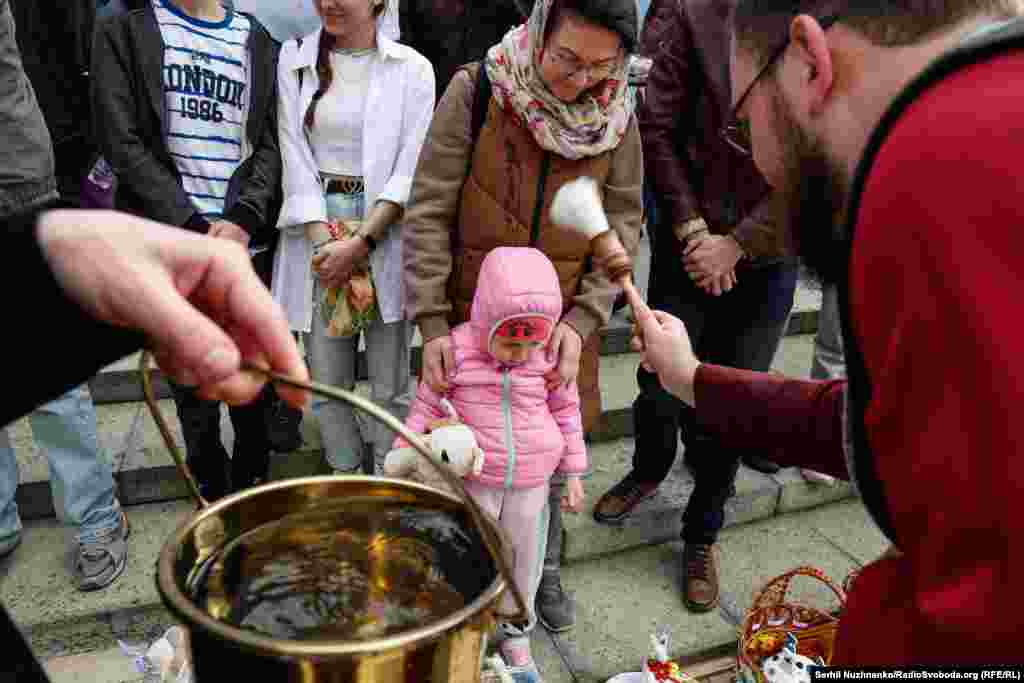 Дівчинка спостерігає за тим, як священник кропить кошики&nbsp;