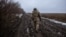 A Ukrainian soldier moves at a position along a tree line on a muddy field.