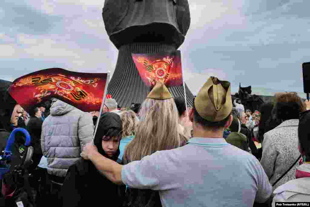 Люди в головных уборах времён Второй Мировой слушают военные песни у Вечного огня