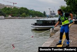 Муниципальный служащий демонстрирует отбор проб воды реки Сены у собора Парижской Богоматери перед Олимпийскими играми в Париже. Франция, 15 июля 2024 года