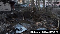 Чоловік стоїть біля вирви у дворі житлового будинку, пошкодженого внаслідок атаки безпілотника в Одесі 17 січня 2024 року