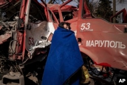 Жінка вкривається ковдрою біля пошкодженої пожежної машини після обстрілу в Маріуполі, 10 березня 2022 року