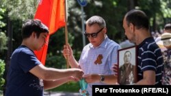 Георгий лентасын тагынган адамга көк лентаны сунуштап жаткан адам. Алматы, 9 май, 2022 жыл.