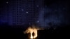 A man stands near burning garbage in front of an apartment building during a scheduled power cut in Kyiv.