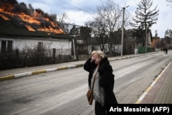 Женщина плачет на фоне горящего дома после обстрела в городе Ирпень под Киевом, 4 марта 2022 года