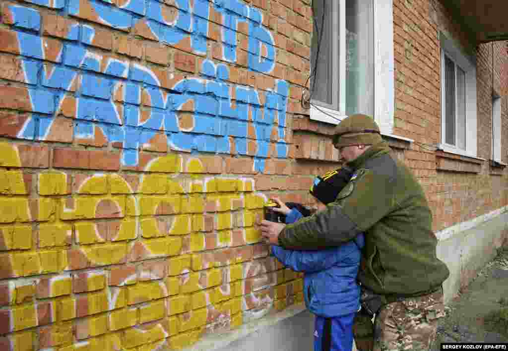 Чоловік і хлопчик розмальовують кольорами українського прапора напис на стіні в Куп&rsquo;янську: &laquo;Любіть Україну. Любіть Шевченка&raquo;