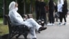 A woman in a face mask and protective suit sits on a bench in central Moscow.