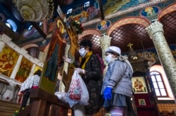 Віряни в захисних масках торкаються розп'яття в одній з православних церков в столиці Північної Македонії Скоп'є. 17 квітня 2020 року