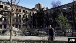 Орусия басып алган Мариуполдо талкаланган үй жана анын жанынан өтүп бараткан тургун.