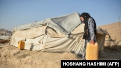 عکس از آرشیف - یک خانم بیجا شده داخلی در افغانستان در حال بردن بشکه آب به خیمه اش در یکی از ولایات افغانستان.