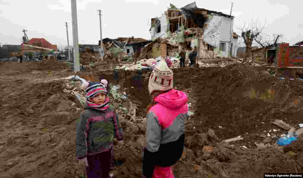 Children stand next to a crater left by a Russian missile strike in the town of Hlevakha, outside Kyiv, on January 26, 2023.