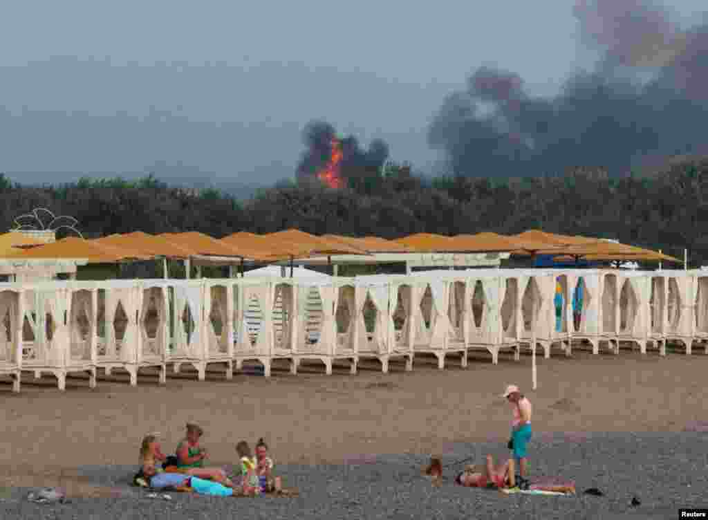 People relax on a beach as smoke and flames rise from a Russian military air base in Ukraine&#39;s occupied Crimea region on August 9, 2022.