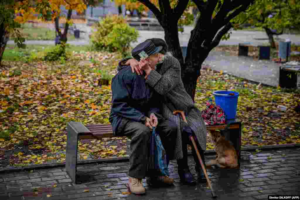 An elderly couple embraces while sitting on a bench in the frontline city of Bakhmut during a lull in shelling on October 27, 2022. The eastern Ukrainian region has been under attack by Russian forces for months.