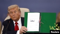 Президент США Дональд Трамп показывает подписанный документ во время саммита по Газе в Шарм-эш-Шейху 13 октября 2025 года