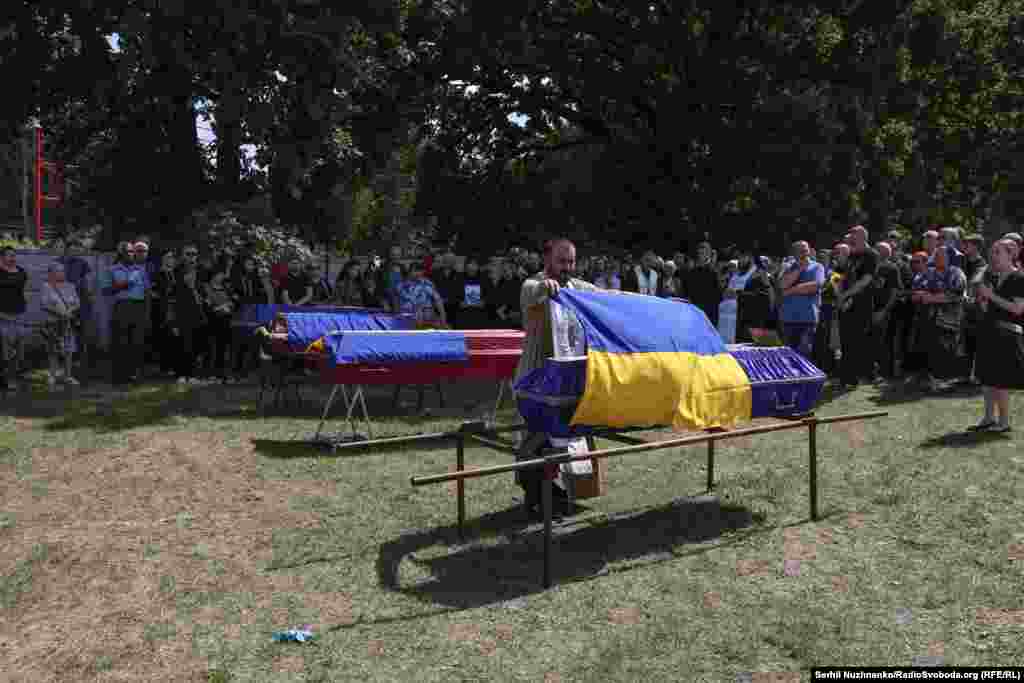 Священник на кладовищі покриває труни прапорами України