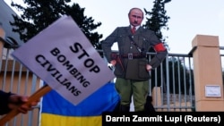 Картонна карикатура на президента Росії Володимира Путіна у вигляді Адольфа Гітлера біля посольства Росії в Республіці Мальта. На плакаті напис англійською: «Припиніть бомбардування мирних жителів». 8 березня 2022 року