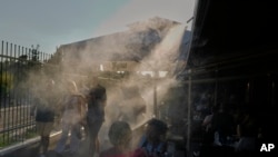 Людзі, каб астудзіцца, праходзяць праз апарат, якія распыляе вільгаць. Атэны, Грэцыя, 1 ліпеня 2025 году