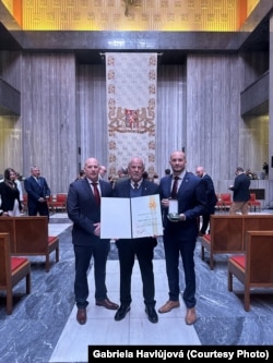 Уручэньне Крыжа абароны дзяржавы адбылося 8 траўня, калі Чэхія, як і астатняя Эўропа, адзначае дзень Перамогі. Унук Сяргей Вайцяхоўскі і яго сыны Майкл і Марк прыехалі з ЗША і Віетнаму