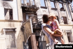 Мама з дитиною біля будівлі в Маріуполі, зруйнованого внаслідок бойових дій у 2014 році, 19 липня 2015 року