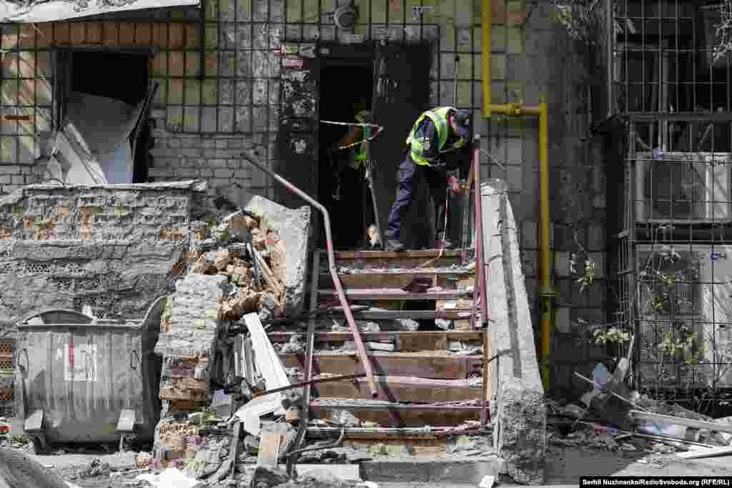 Поліцейські натягують захисну стрічку на пошкоджені вибухом двері та сходи, що ведуть до одного з під'їздів житлового будинку в Солом'янському районі, в який поцілила російська ракета