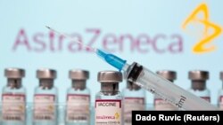 Vials labeled "AstraZeneca COVID-19 Coronavirus Vaccine" and a syringe are seen in front of a displayed AstraZeneca logo, March 10, 2021.