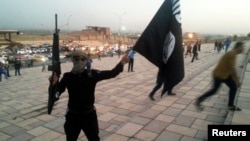 «Ирак пен Шам ислам мемлекеті» (ИЛИМ) ұйымының туын ұстап тұрған қарулы адам.  Мосул, Ирак, 23 маусым 2014 жыл.