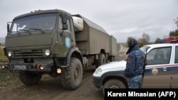 NAGORNO-KARABAKH -- A Karabakh Armenian police officer patrols as a truck of Russian peacekeeping forces moves past him at their checkpoint outside Askeran, November 20, 2020