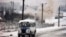 A bus drives past as smoke rises from a building that had been repeatedly hit by tank shells in the southwest of Grozny in January 1995.