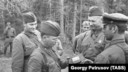 Советтик жазуучулар: Михаил Шолохов (биринчи катарда солдо), Евгений Петров жана Александр Фадеев (экинчи катарда турушат) талкаланган немис танкынан алынган буюмду көрүп атышат. 1941-жыл.