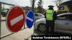 Милиция кызматкери Бишкек шаарынын кире беришине орнотулган блокпостто айдоочуларды текшерип жатат.25-март, 2020-жыл.