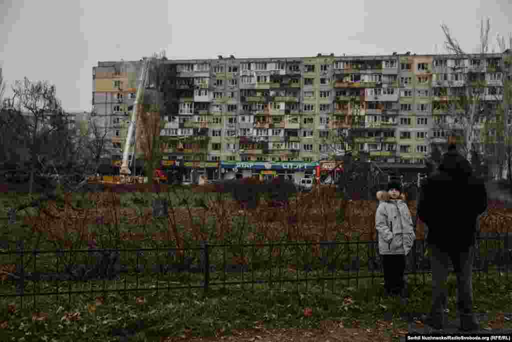 З безпечної відстані за роботою працівників ДСНС після російського обстрілу спостерігає і хлопчик з татом. Київ, Дарницький район, 29 листопада 2025 року