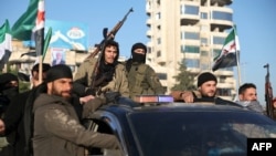 Anti-government fighters brandish their guns as they ride a vehicle in Syria's northern city of Aleppo on November 30, 2024.