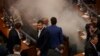 Kosovo lawmakers stand amid tear gas after canisters were released by opposition lawmakers during a parliament session in Pristina on March 21.