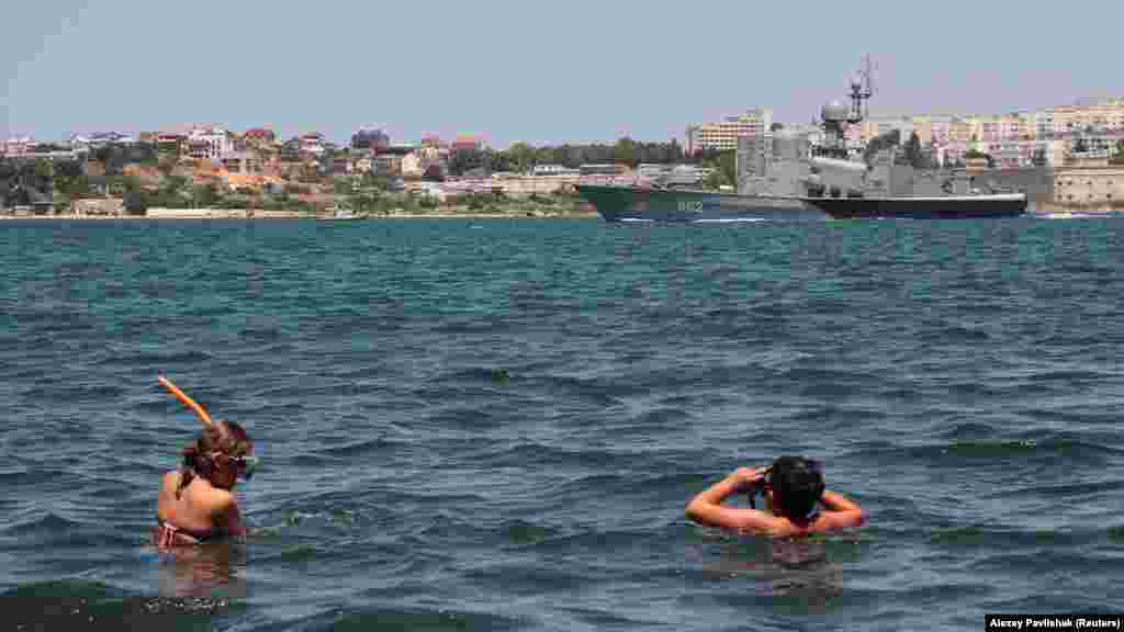 Відпочивальники дивляться на навчання військових кораблів Чорноморського флоту Росії в анексованому Севастополі