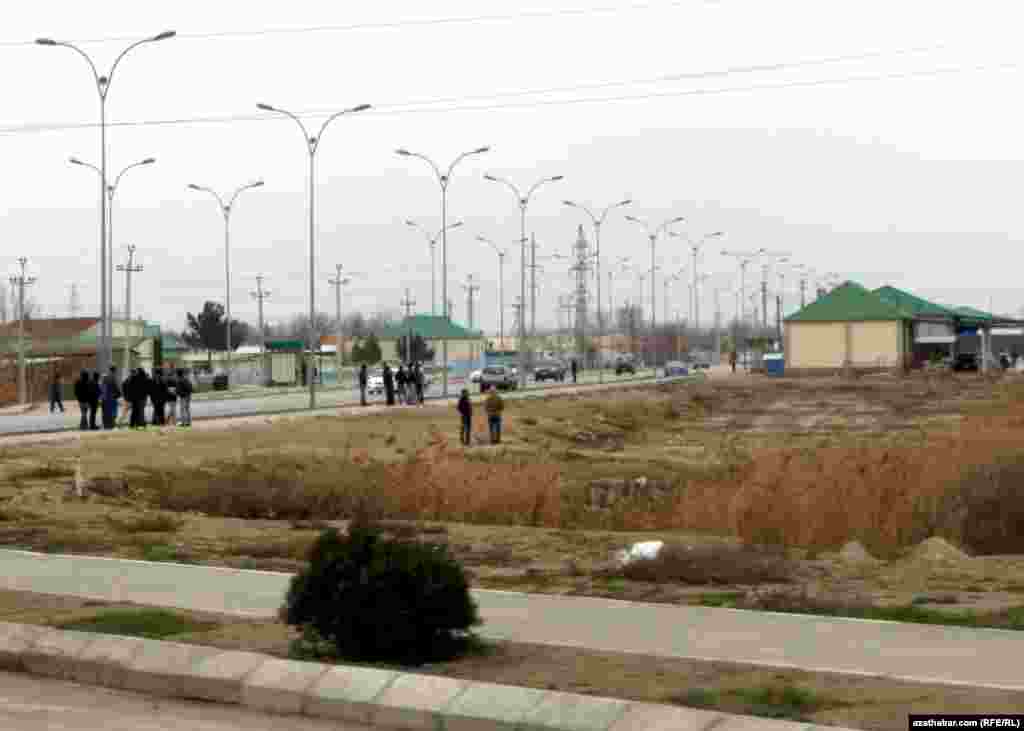 Aşgabadyň Garadamak obasyna barýan ýolda awtobusa garaşýan ýolagçylar. Bu ýerde awtobus duralgasy bolmany sebäpli, ýolagçylar köçäniň ugrunda awtobusa garaşýarlar.