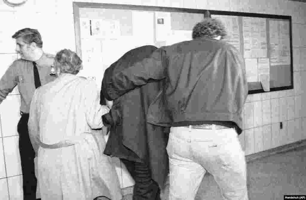 Марку Чепмену (на фото в центрі), підозрюваному у вбивстві Джона Леннона, наділи бронежилет і накинули на голову пальто, щоб ніхто не бачив його обличчя, і таким чином доправили його з поліцейського відділку в кримінальний суд Нью-Йорка