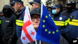 A woman with the EU and Georgian flags stands in front of police blocking a street during a an opposition rally in Tbilisi. (file photo)