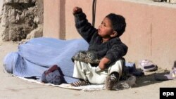 یکی از زنان نیازمند که با فرزند خود در روی یکی از جاده ها خیرات جمع می کند