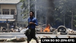 Янгон шаарында жоокерлер өрттөп салган баррикаданын жанынан качып бараткан киши. Бирма. 2021-жылдын 10-марты.