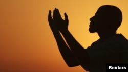 Мужчина поднимает руки, чтобы помолиться у моря на закате, после целого дня поста в священный месяц Рамадан в Бенгази, Ливия. 